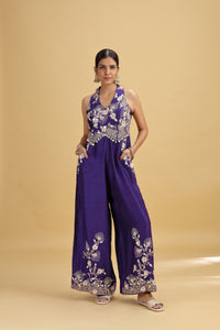 Woman wearing a purple embroidered jumpsuit on a beige background