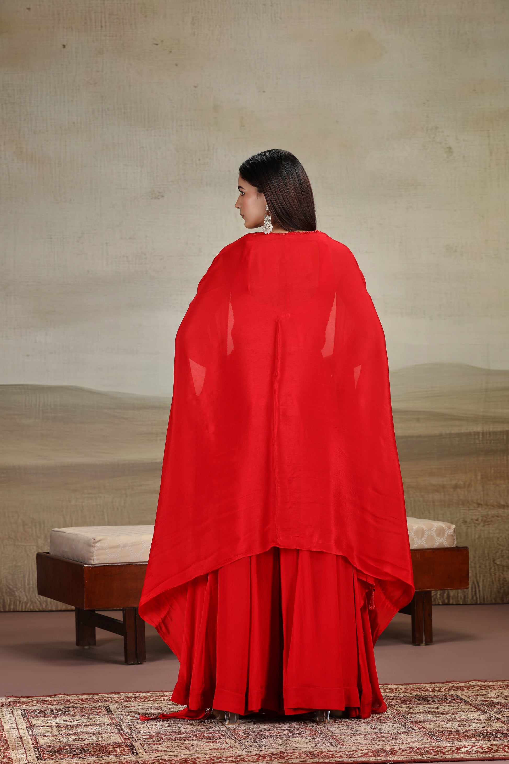 Woman wearing a red salwar suit standing in front of a textured wall.