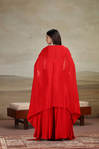 Woman wearing a red salwar suit standing in front of a textured wall.