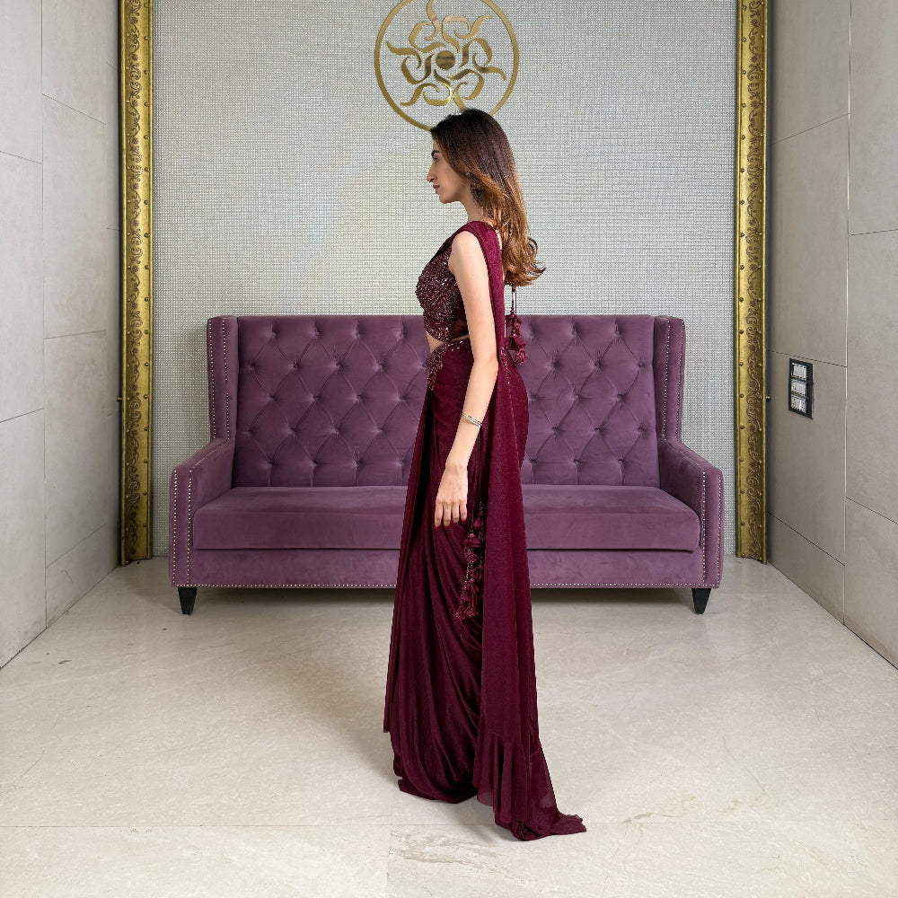 Woman in a red crepe saree standing next to a purple couch in a room with gold trim.