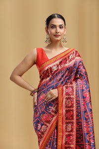 Woman wearing a traditional patola saree with a red and blue pattern on a beige background