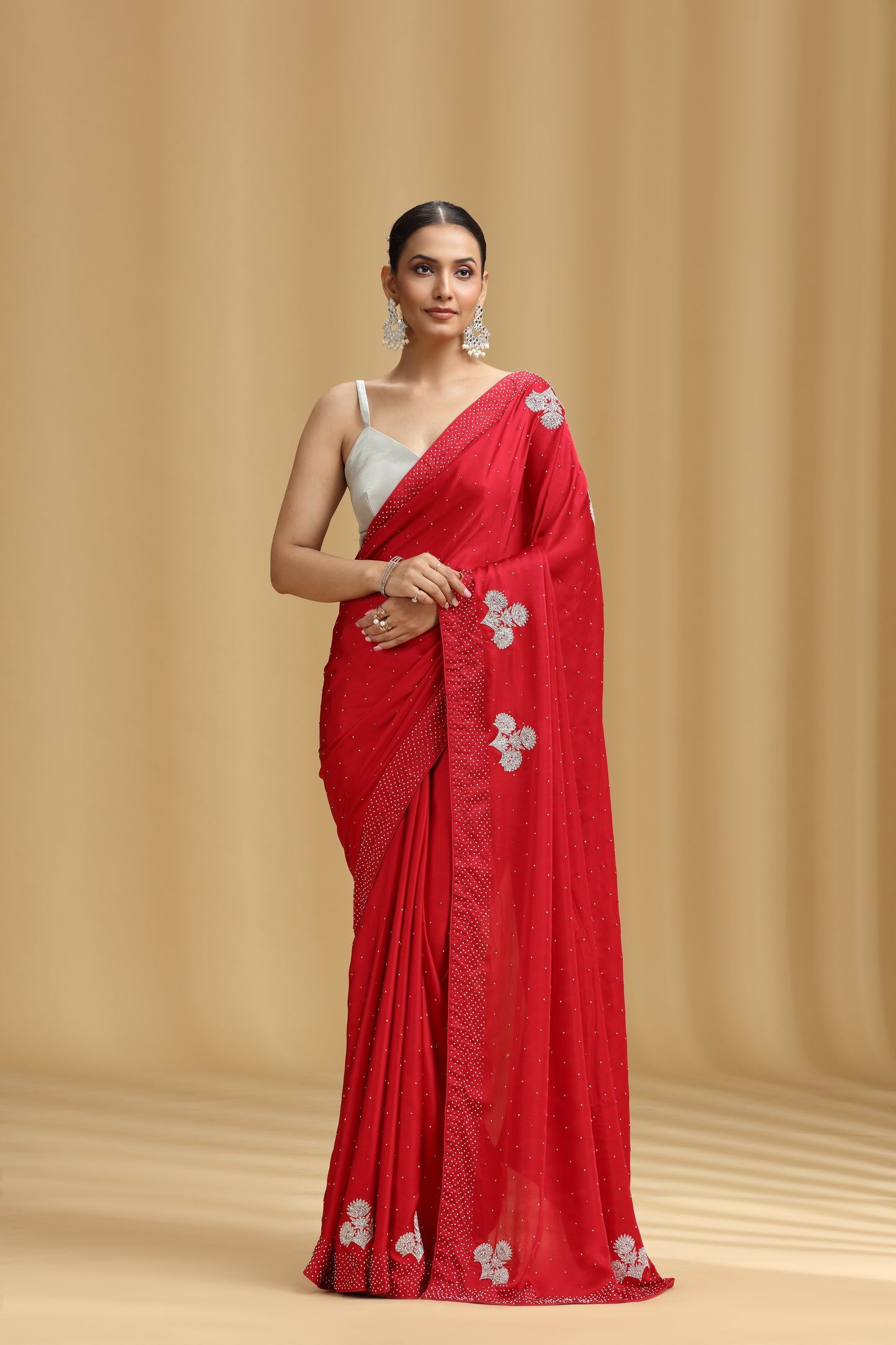Woman wearing a red satin saree with white floral patterns on a beige background