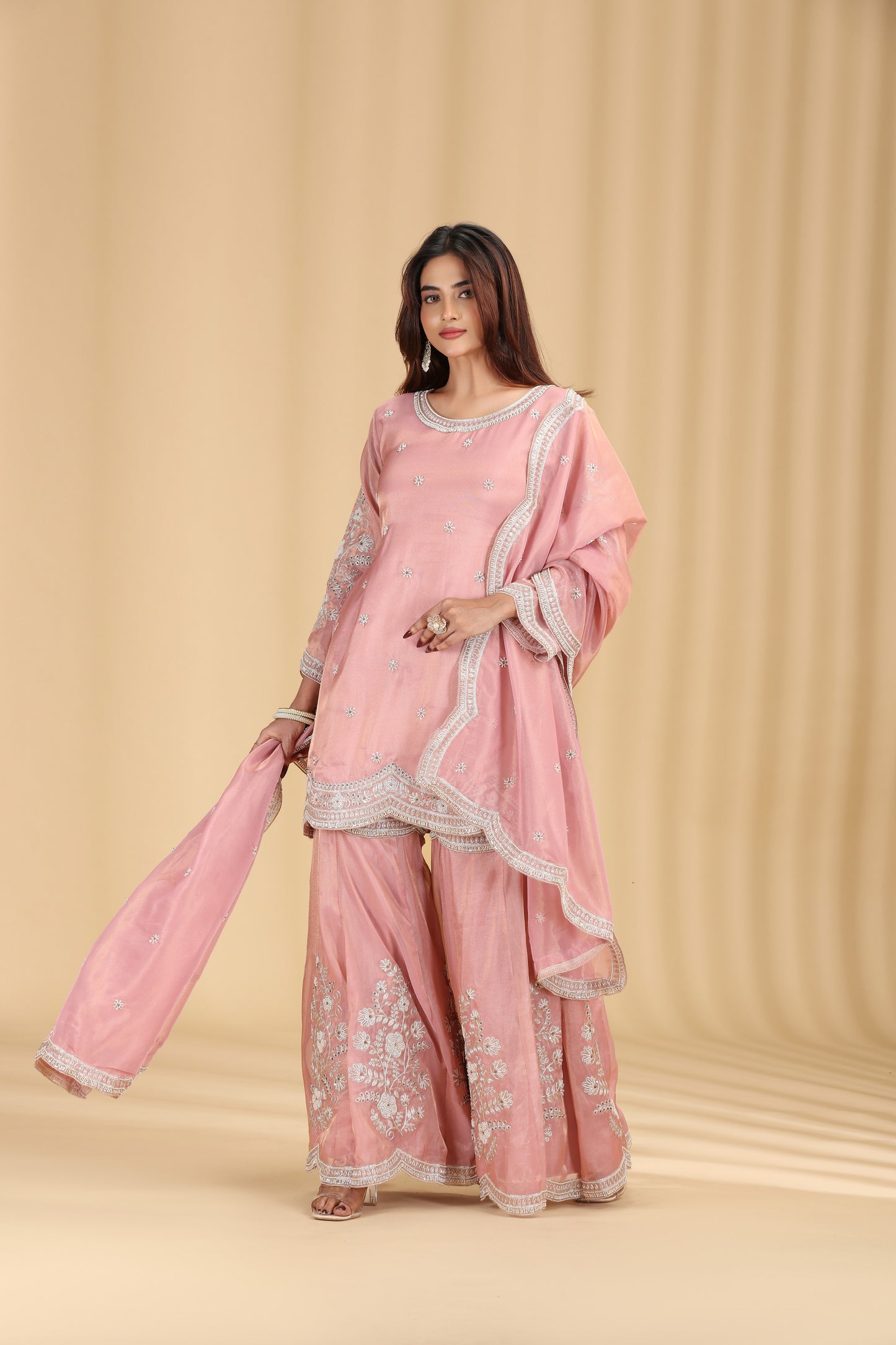 Woman wearing a pink traditional outfit with white embroidery on a beige background