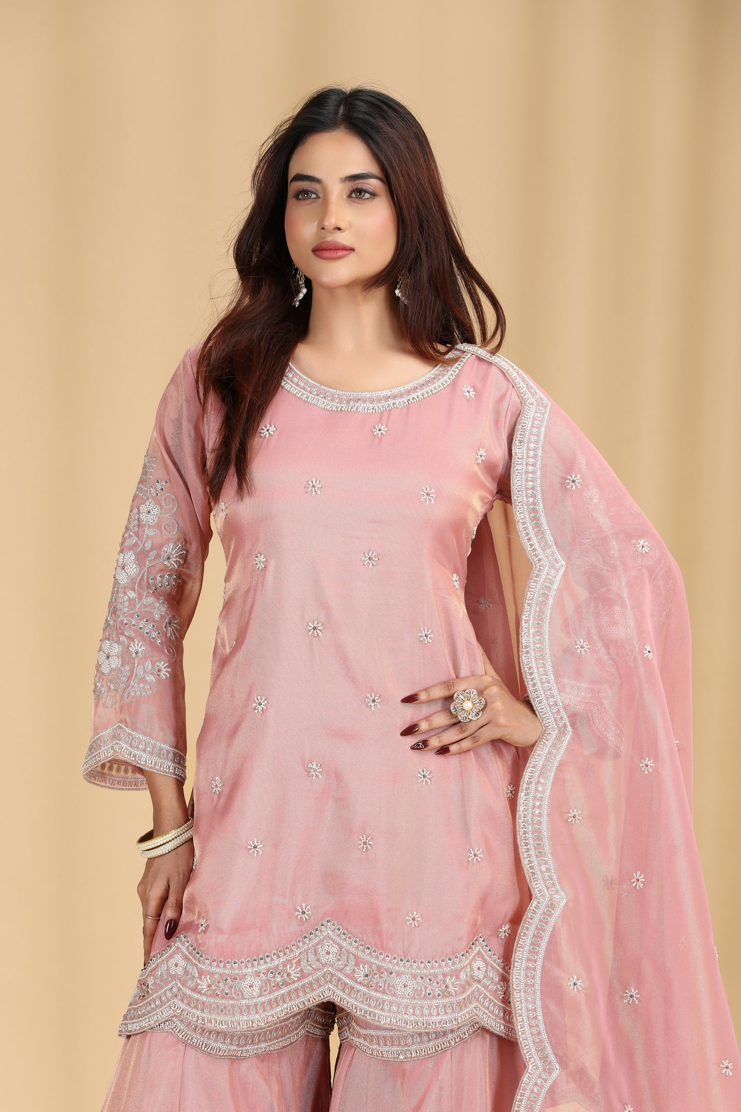 Woman wearing a pink traditional salawar suit outfit with intricate designs on a beige background