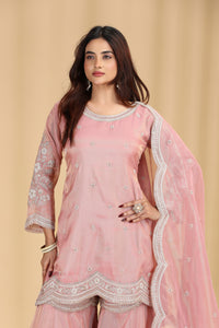 Woman wearing a pink traditional salawar suit outfit with intricate designs on a beige background
