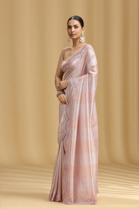 Woman wearing a light pink saree with a subtle pattern on a beige background