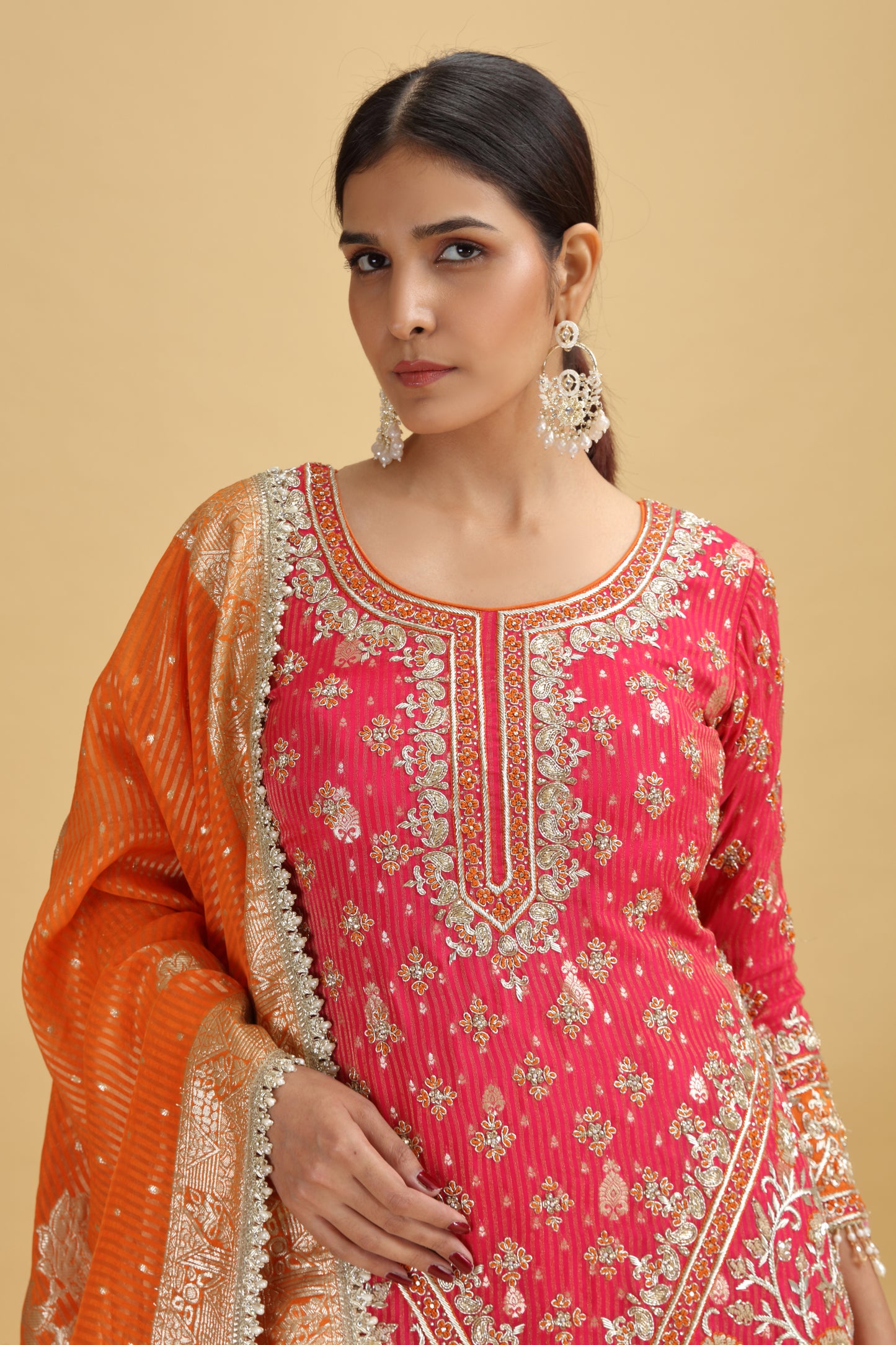 Woman wearing a pink and orange salwar kameez suit embroidery on a beige background