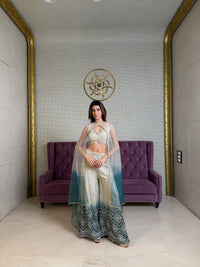 Woman in a white & green salwar standing next to a purple couch in a room with gold accents.