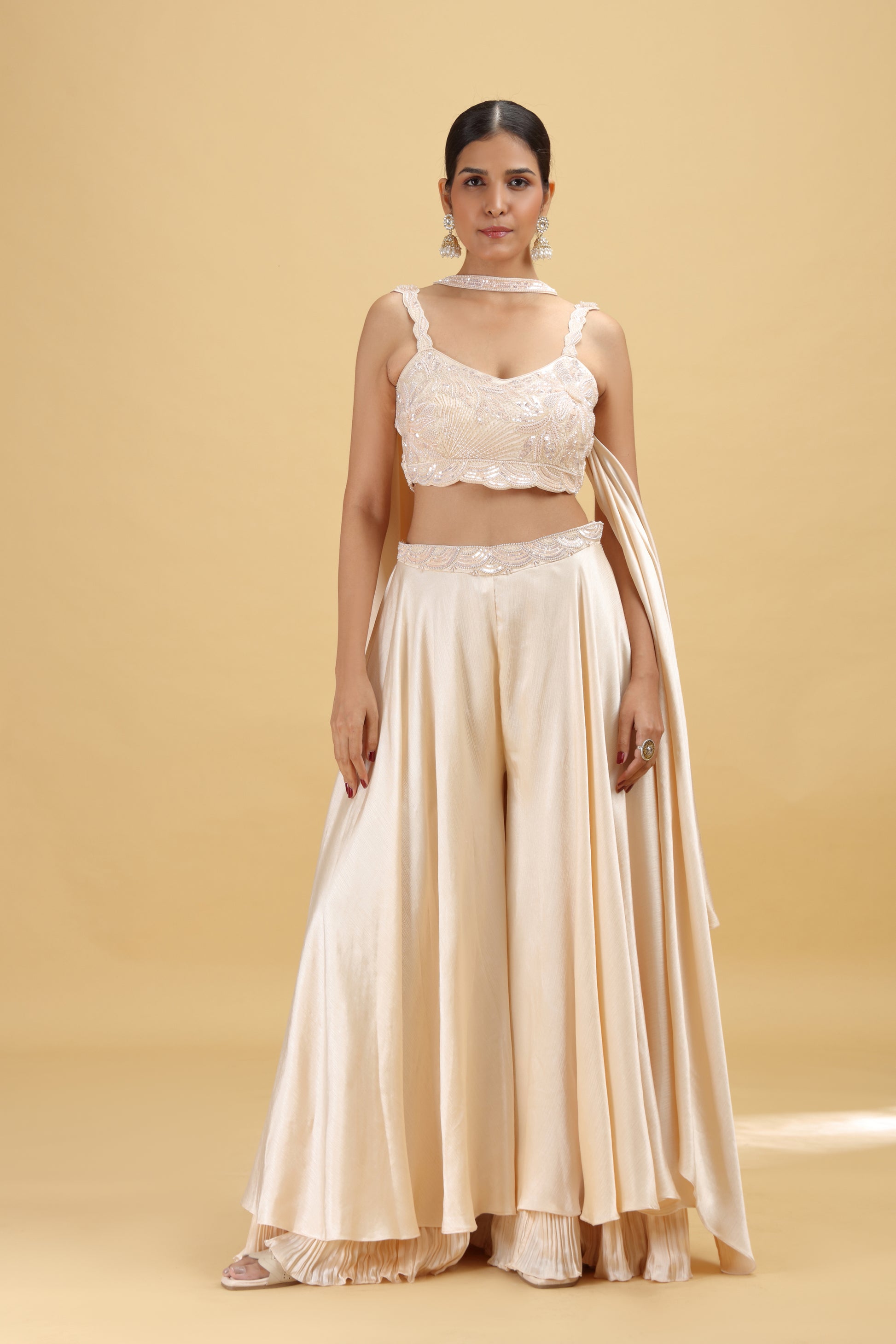 Woman wearing a beige chiffon suit with a lace top and flowing skirt on a beige background