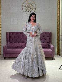 Woman in a grey net lehenga standing in a room with a purple couch and decorative wall.