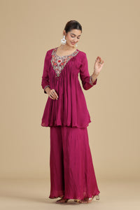 Woman wearing a magenta kurta set with embroidery on a beige background