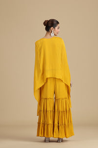 Woman wearing a mustard yellow kurta set with a layered skirt against a beige background