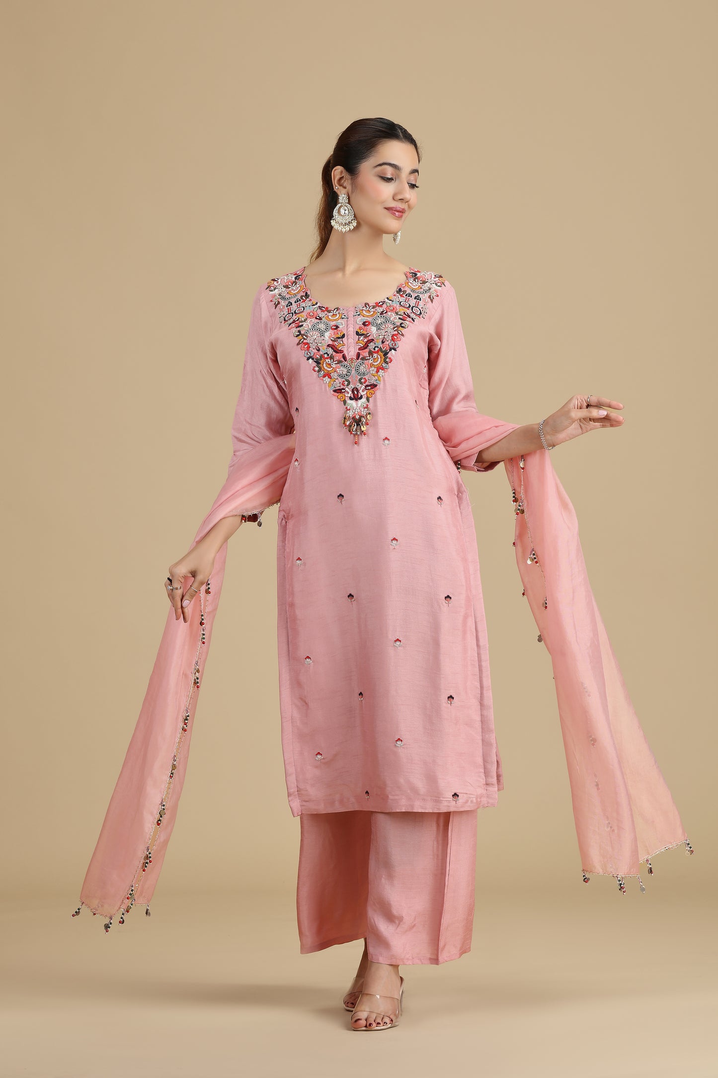 Woman wearing a peach kurta embroidered traditional outfit with a beige background