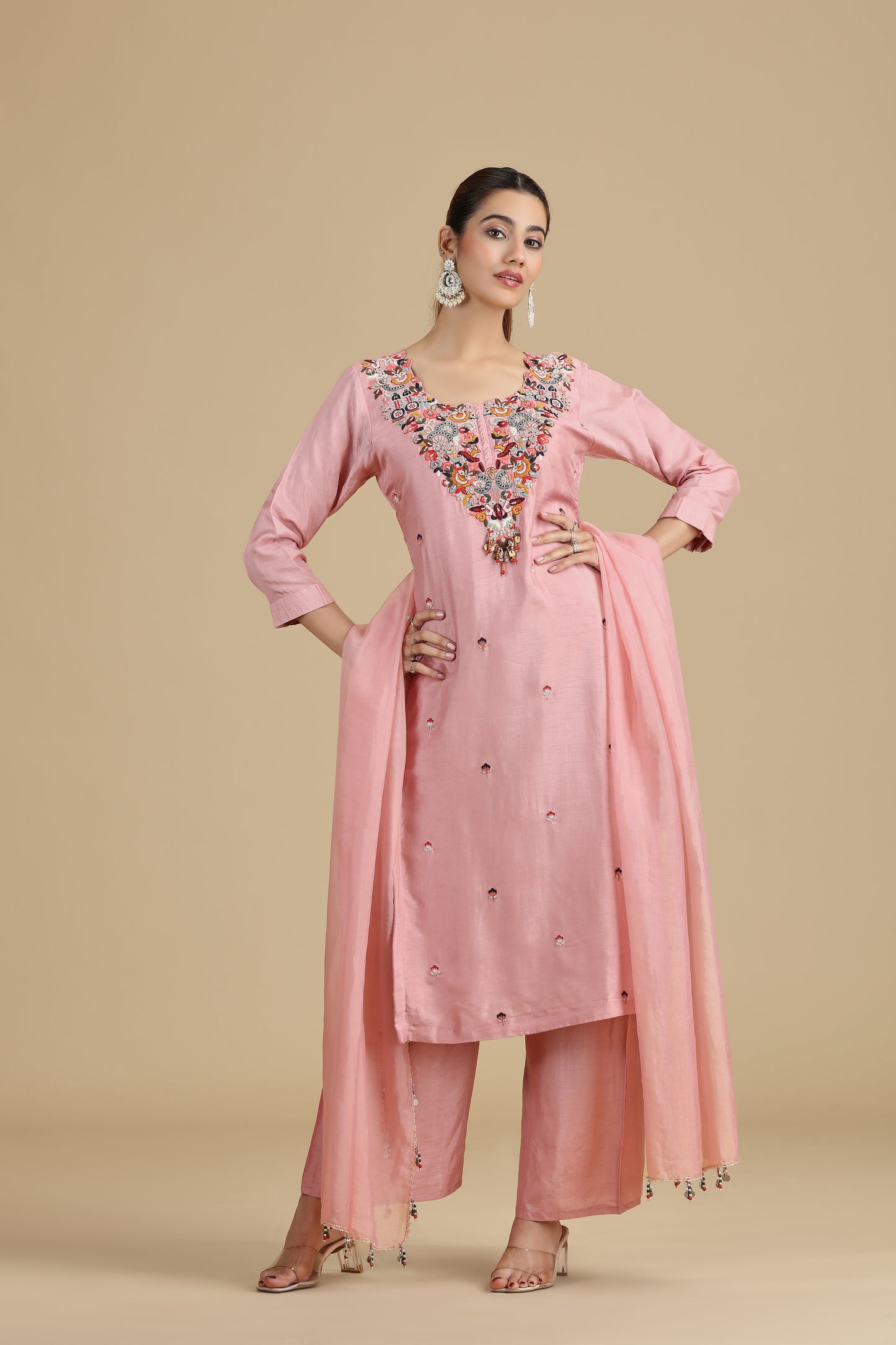 Woman wearing a peach embroidered traditional outfit on a beige background
