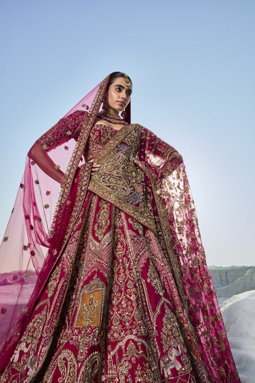 Woman in a traditional embroidered pink and gold lehenga against a clear blue sky.