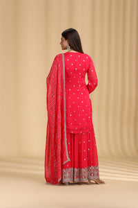 Woman wearing a rani pink traditional outfit with a beige background giving a back pose