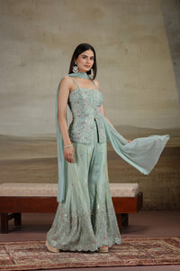 Woman in a pista green tissue suit set with sequins and thread embroidery with a matching dupatta against a neutral background