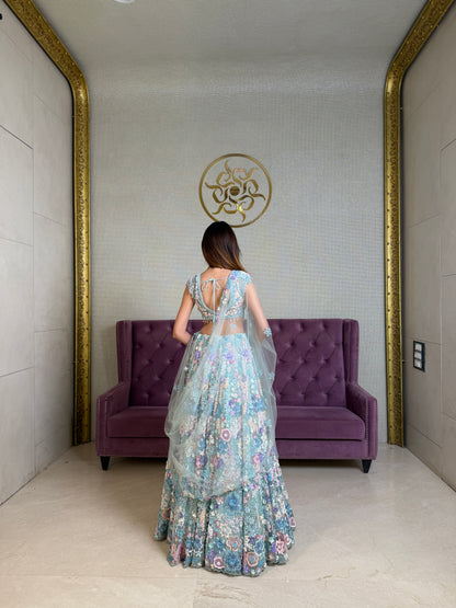 Woman in a powder blue net bridal lehenga standing in front of a purple couch 