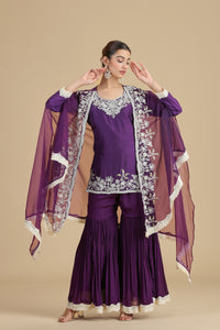 Woman wearing a purple kurta set with white embroidery on a beige background