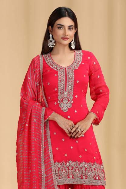 Woman wearing a rani pink suit with silver embroidery on a beige background